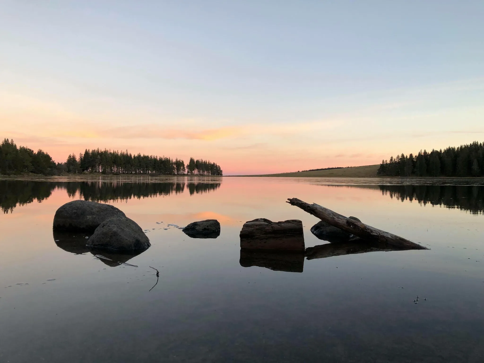 Paysage apaisant d'un lac paisible au coucher du soleil avec reflets d'arbres et rochers