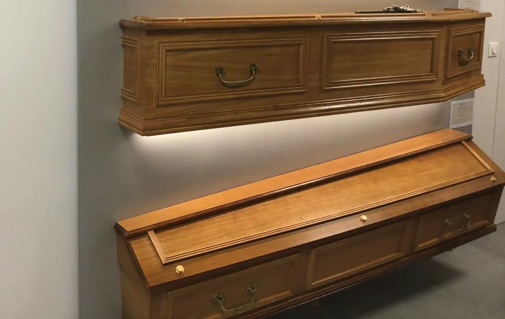 Exposition de cercueils traditionnels en bois noble sur supports muraux dans un showroom funéraire