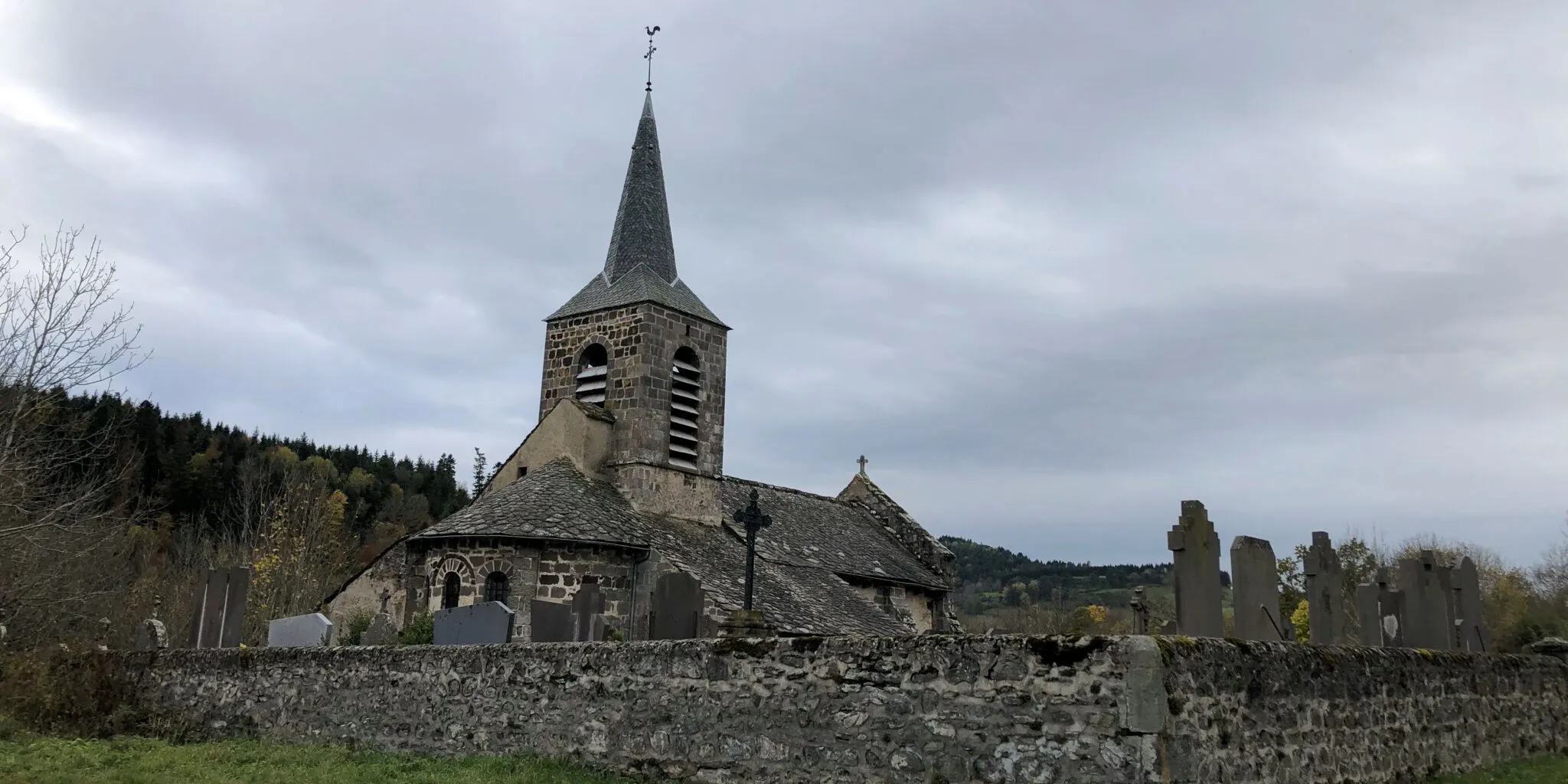 Ancienne église en pierre entourée d'un cimetière avec stèles funéraires sous un ciel nuageux
